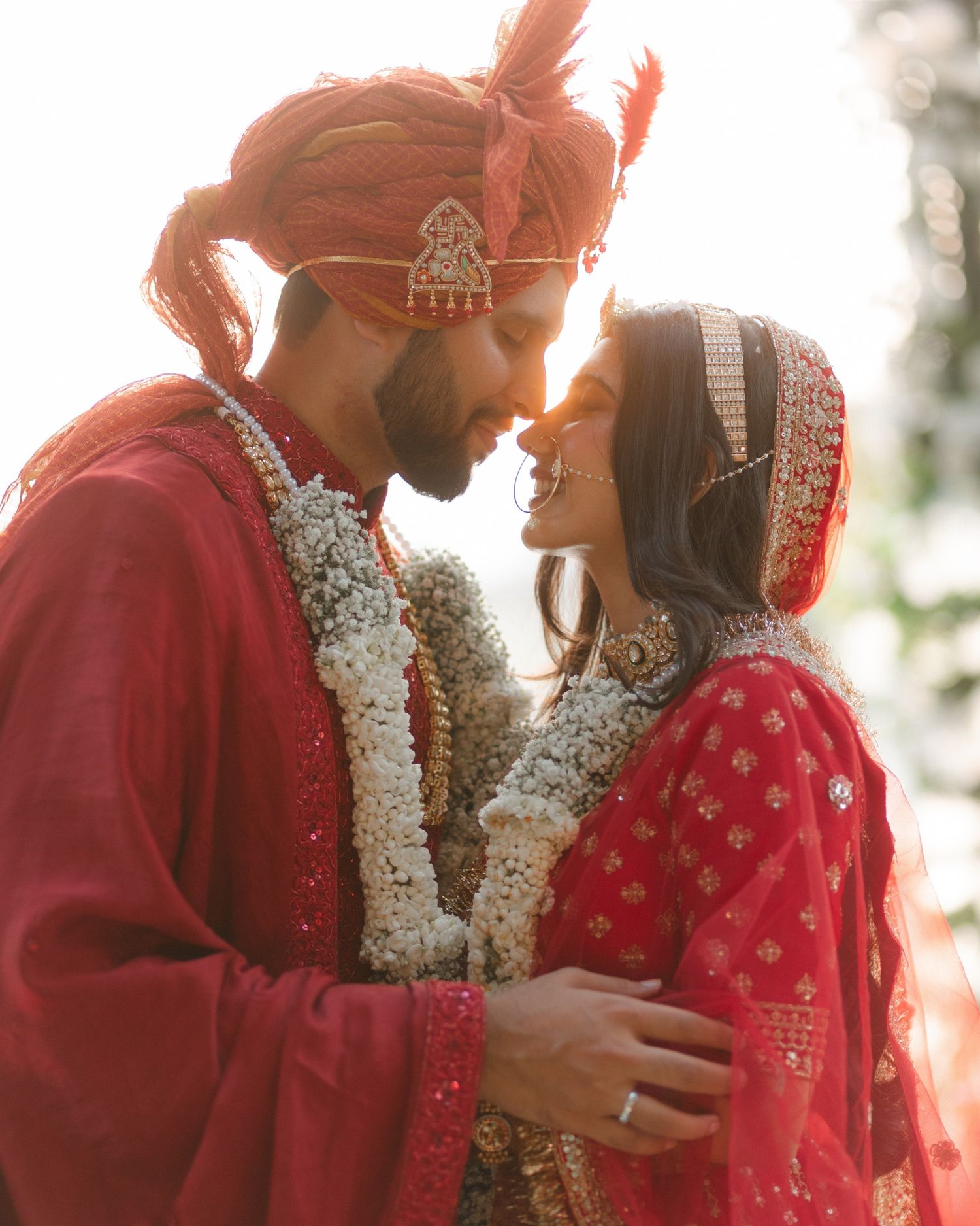 Indian bride and groom in traditional red wedding attire with floral garlands sharing an intimate moment.