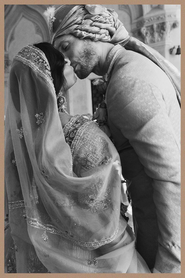 Black and white intimate photo of Indian bride and groom sharing a kiss in traditional wedding attire.
