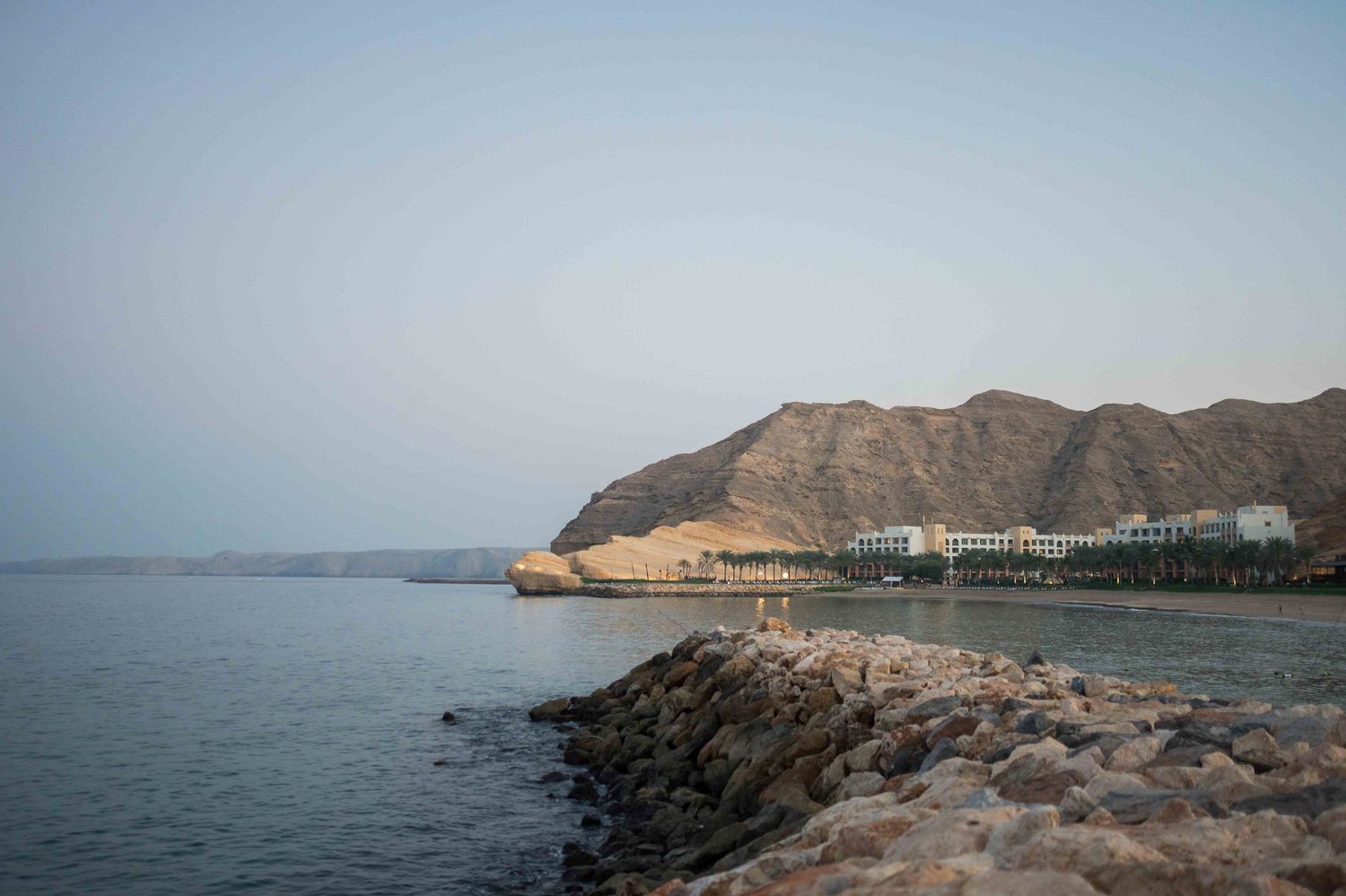 Scenic coastal view of rocky shoreline with white buildings nestled against rugged mountain cliffs.