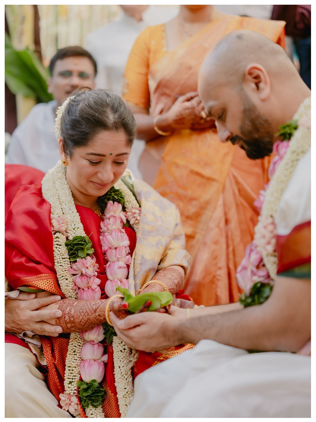 Emotional bride in red saree and groom perform traditional South Indian wedding ritual with flower offerings together.