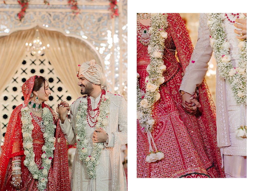 Indian bride in red lehenga and groom in cream sherwani exchanging floral garlands at wedding ceremony.
