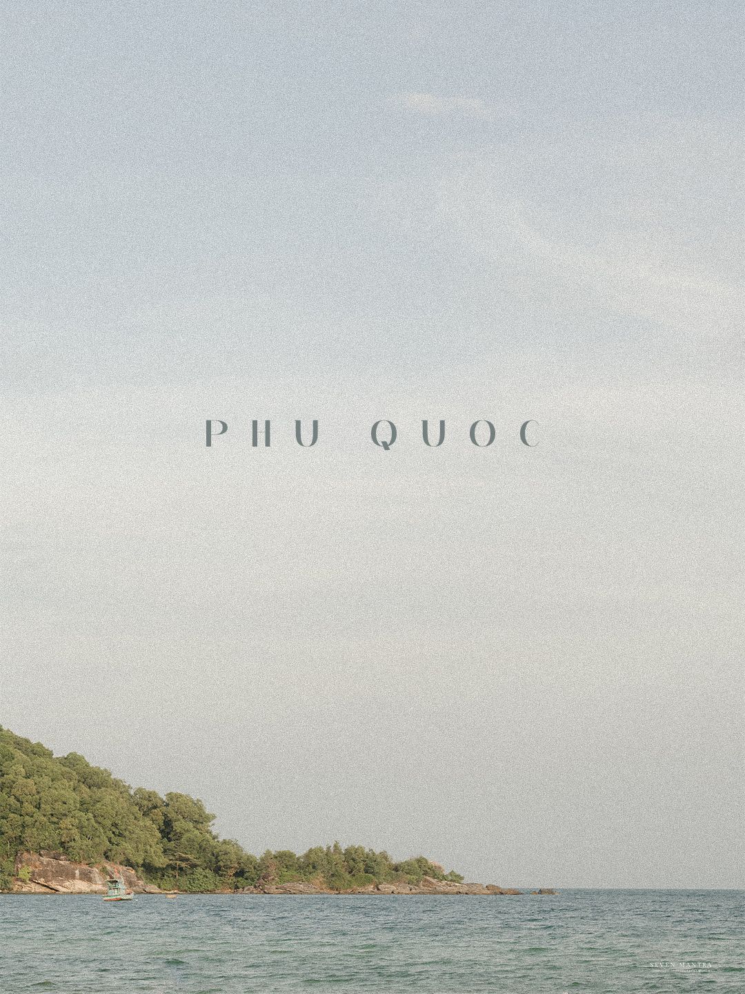 Serene coastal landscape of Phu Quoc island with turquoise waters and lush green trees under pale sky.