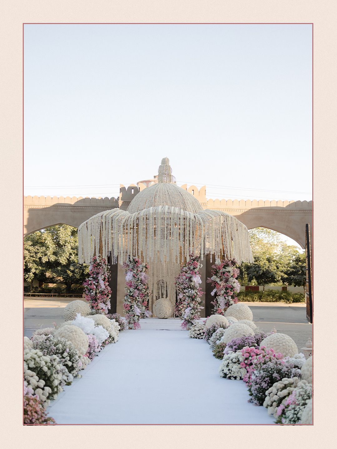 Elegant wedding mandap with crystal fringe canopy lined with pink and white floral arrangements.