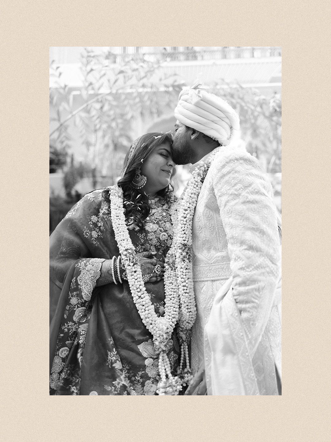 Black and white portrait of Indian bride and groom exchanging garlands at wedding ceremony.