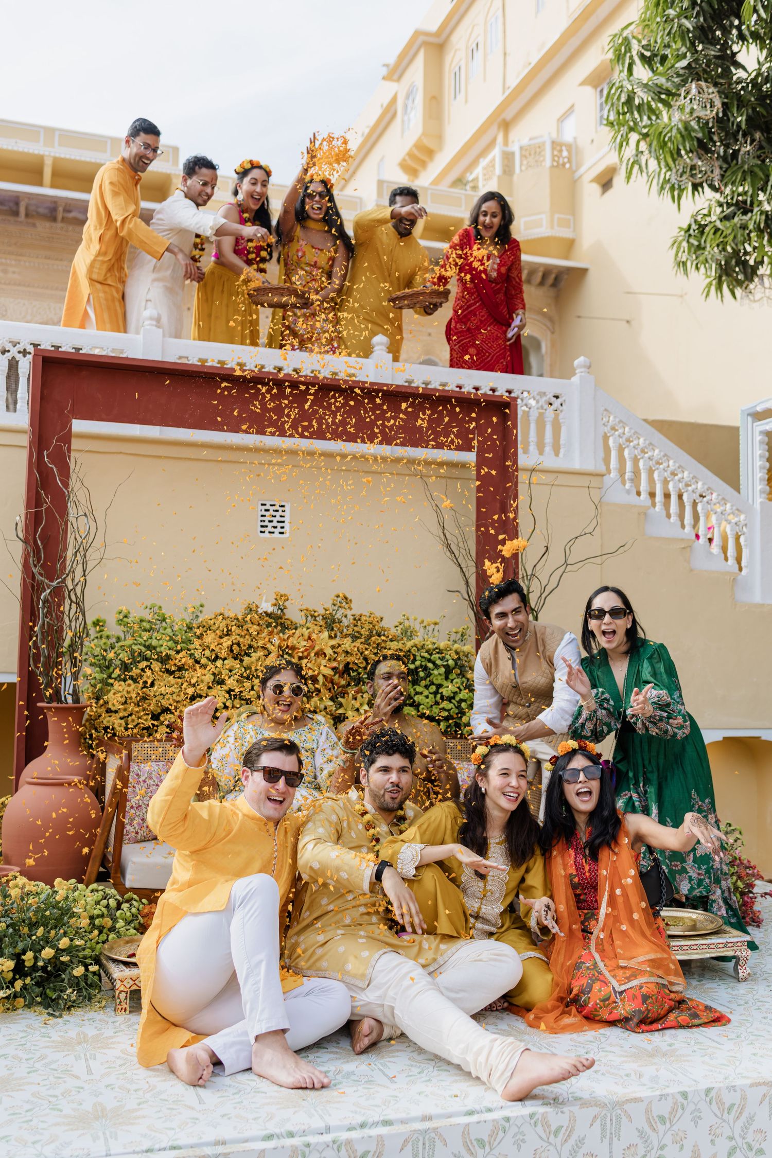 Wedding party throws marigold petals in a lively group photo at an Indian haldi ceremony.