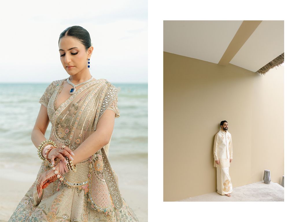Indian bride in ornate gold lehenga with sapphire jewelry poses by ocean alongside groom in white kurta.