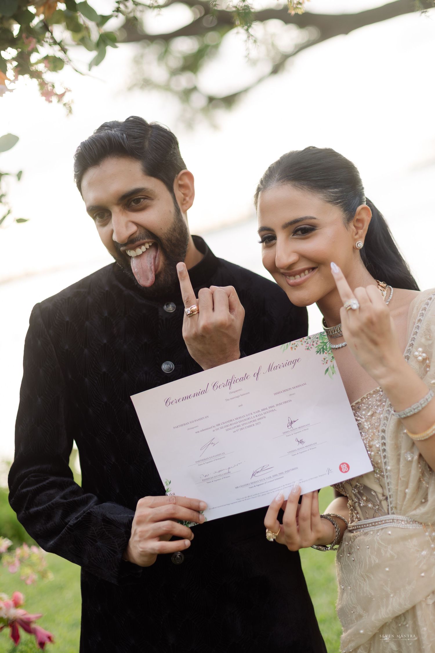 Newlywed Indian couple joyfully display their marriage certificate and wedding rings outdoors.