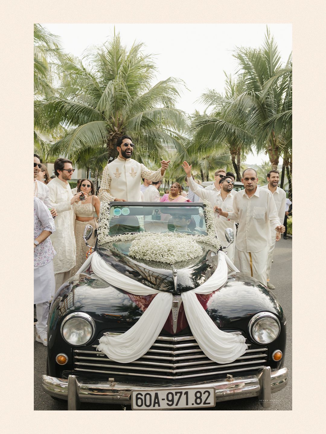 Groom arrives in a decorated vintage black convertible car during Indian wedding baraat procession.