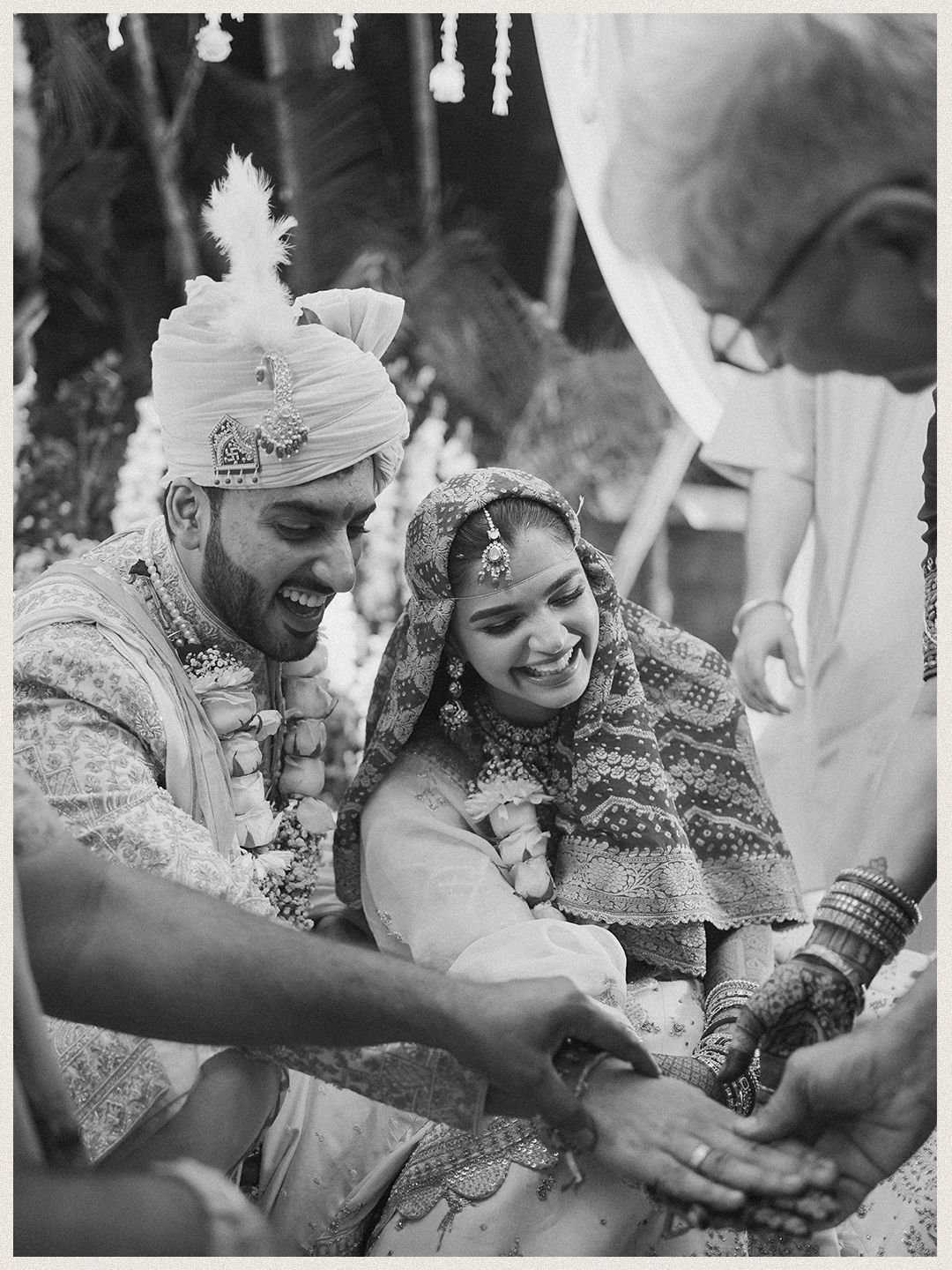 Black and white candid photo of laughing Indian bride and groom during traditional wedding rituals.