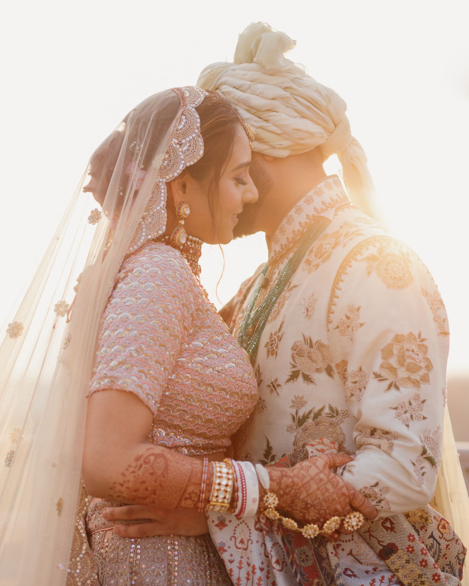 Indian wedding couple sharing a romantic moment under a veil with golden backlight, bride in pink lehenga.