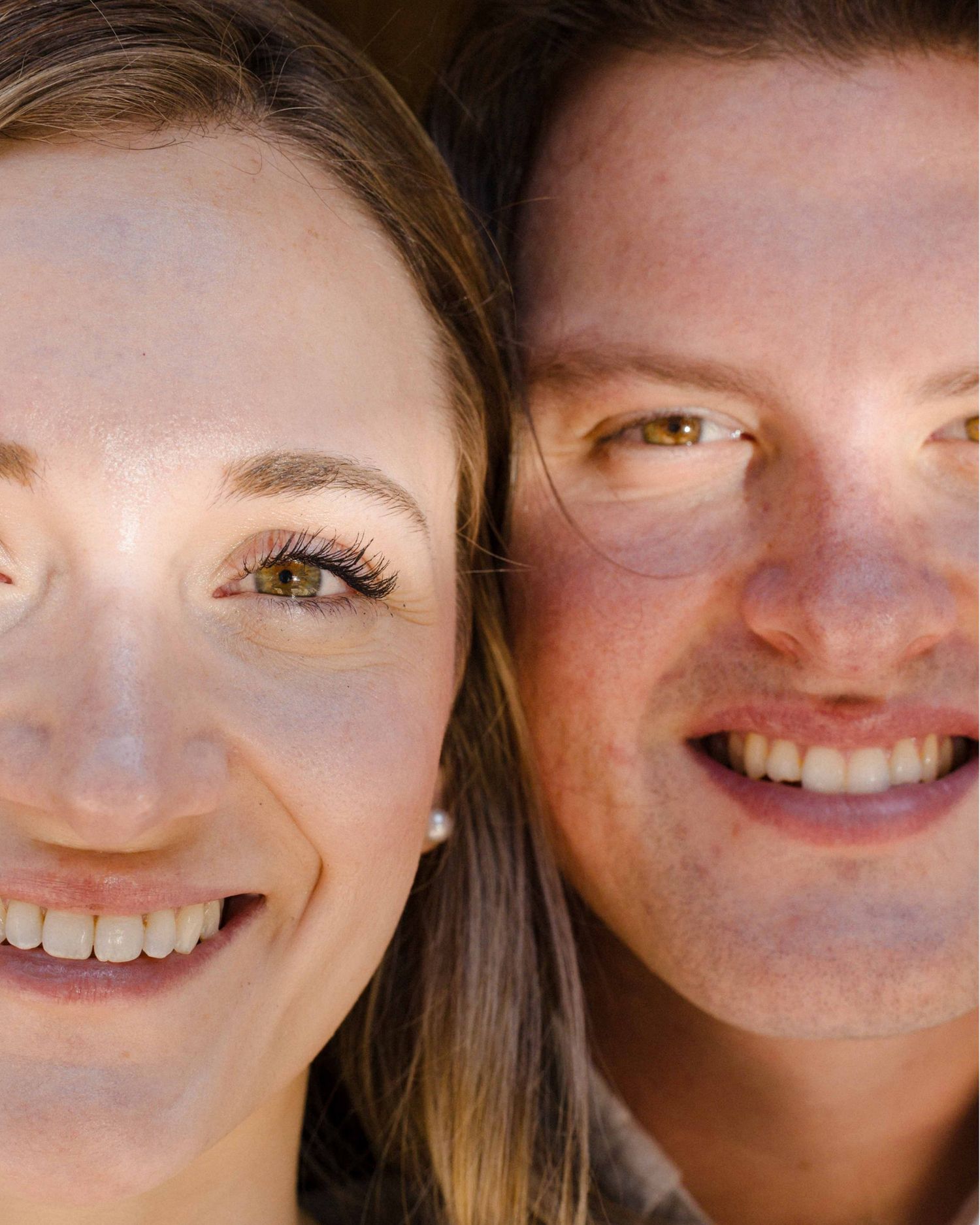Close-up portrait of smiling couple with freckles and warm expressions in natural light.