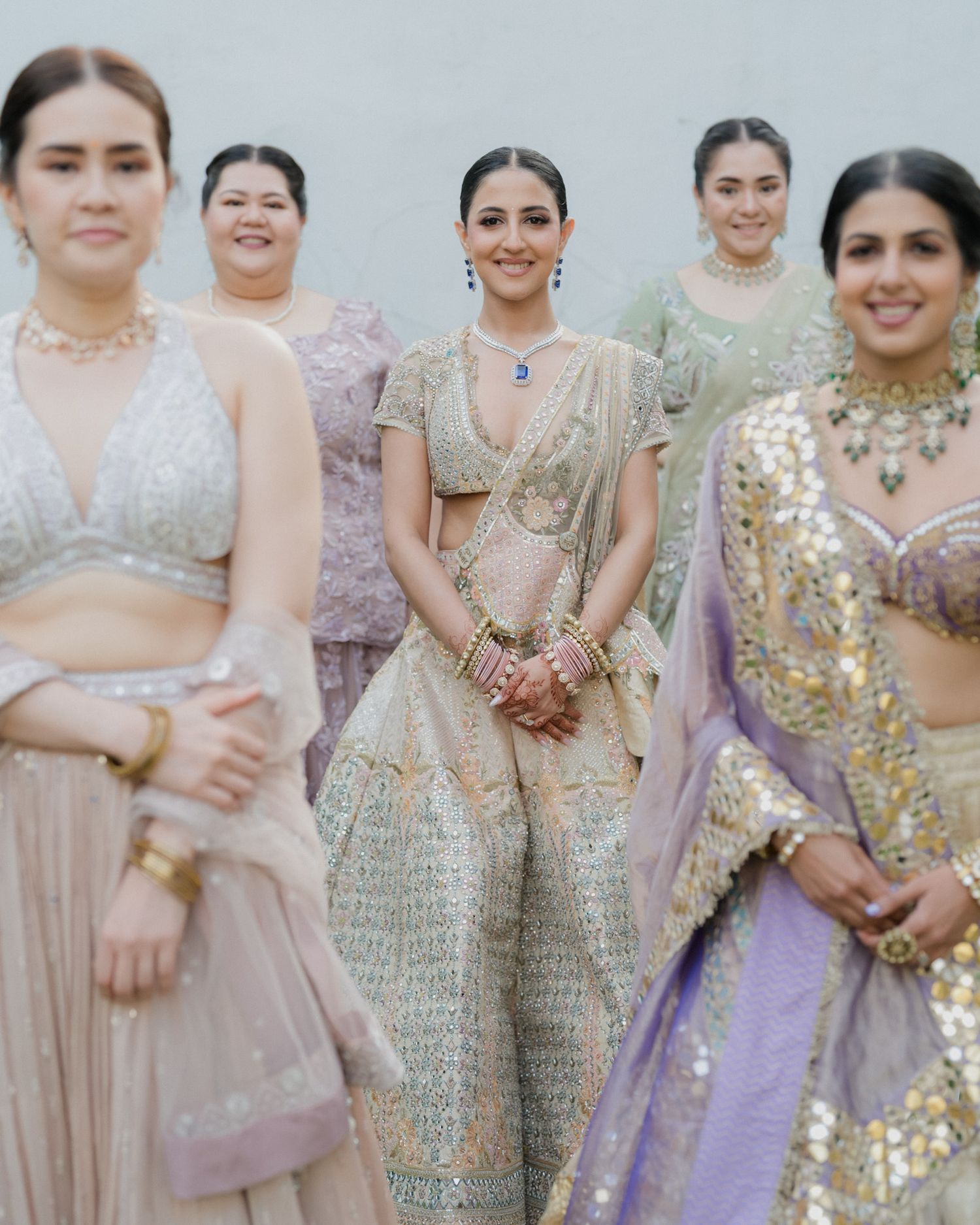 Indian bride in silver embroidered lehenga smiling with bridesmaids in colorful traditional attire.