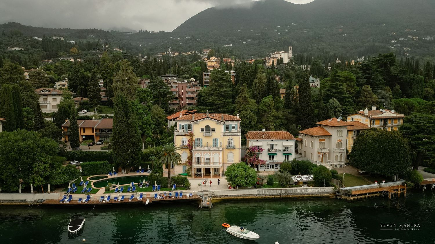 Aerial view of elegant lakeside villa surrounded by lush trees and mountains at Lake Como, Italy.