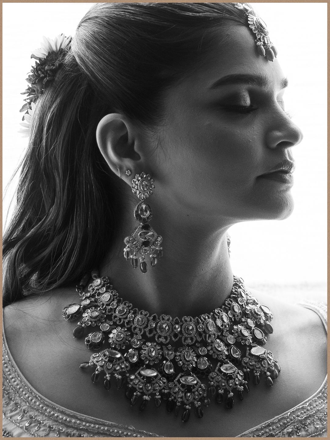 Black and white close-up profile of Indian bride wearing an ornate statement necklace, chandelier earrings, and maang tikka.