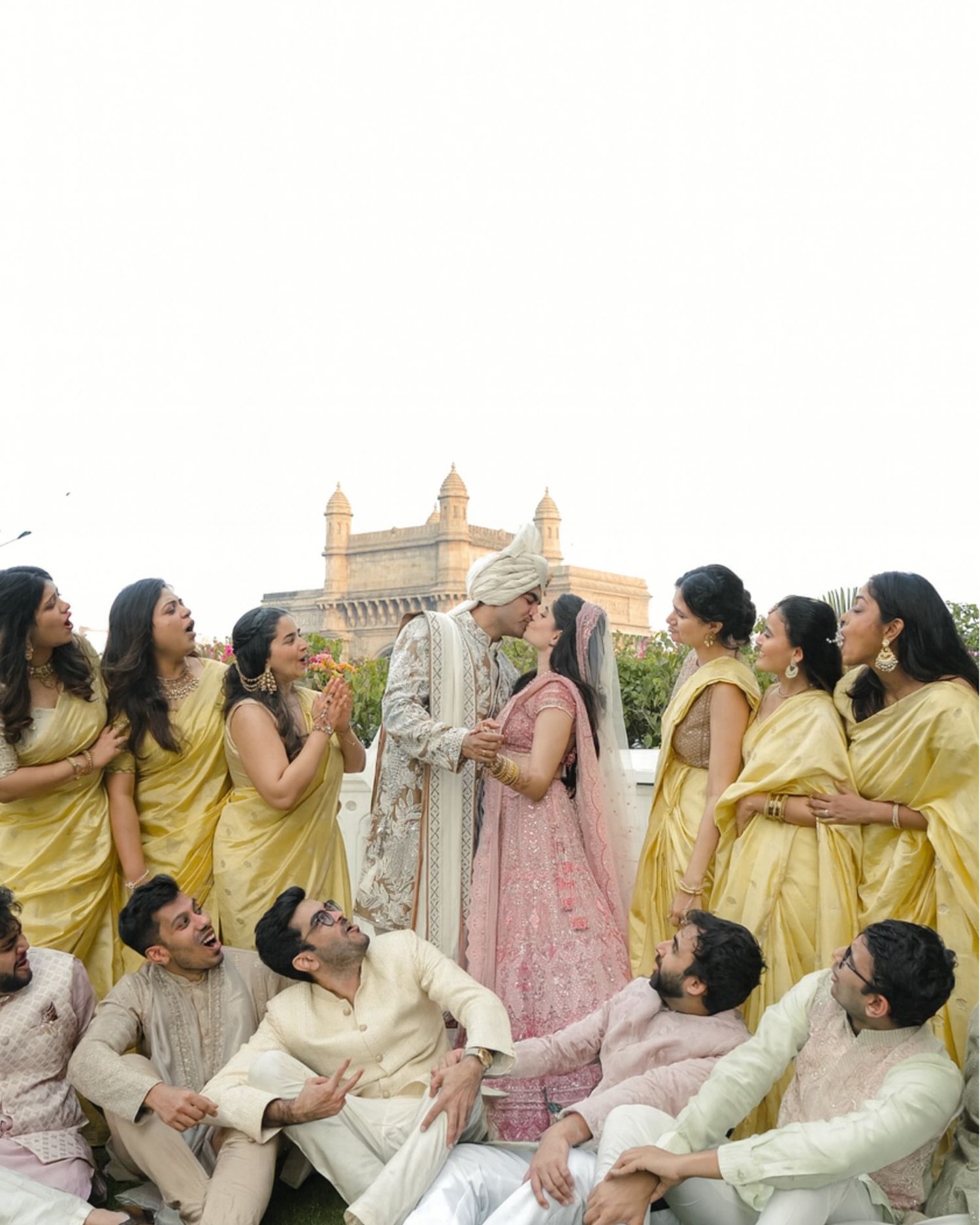 Indian wedding couple surrounded by bridesmaids in yellow sarees and groomsmen at Gateway of India Mumbai.