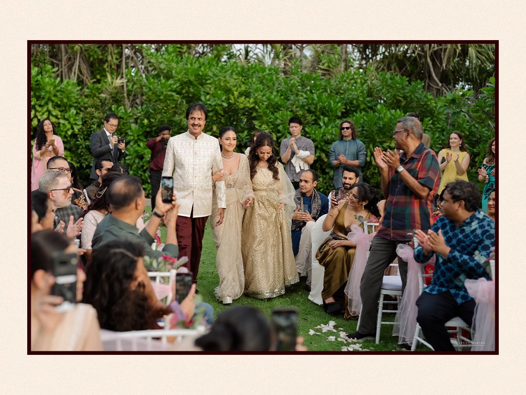Bride and groom walking down the aisle at an outdoor garden wedding ceremony with guests applauding.