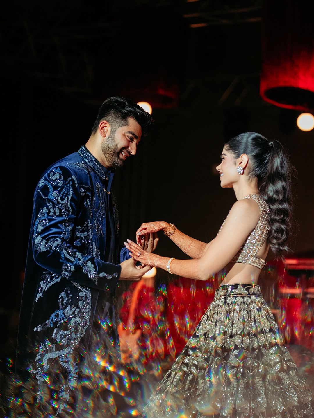 Couple exchanging rings at engagement ceremony, groom in blue sherwani and bride in gold lehenga.
