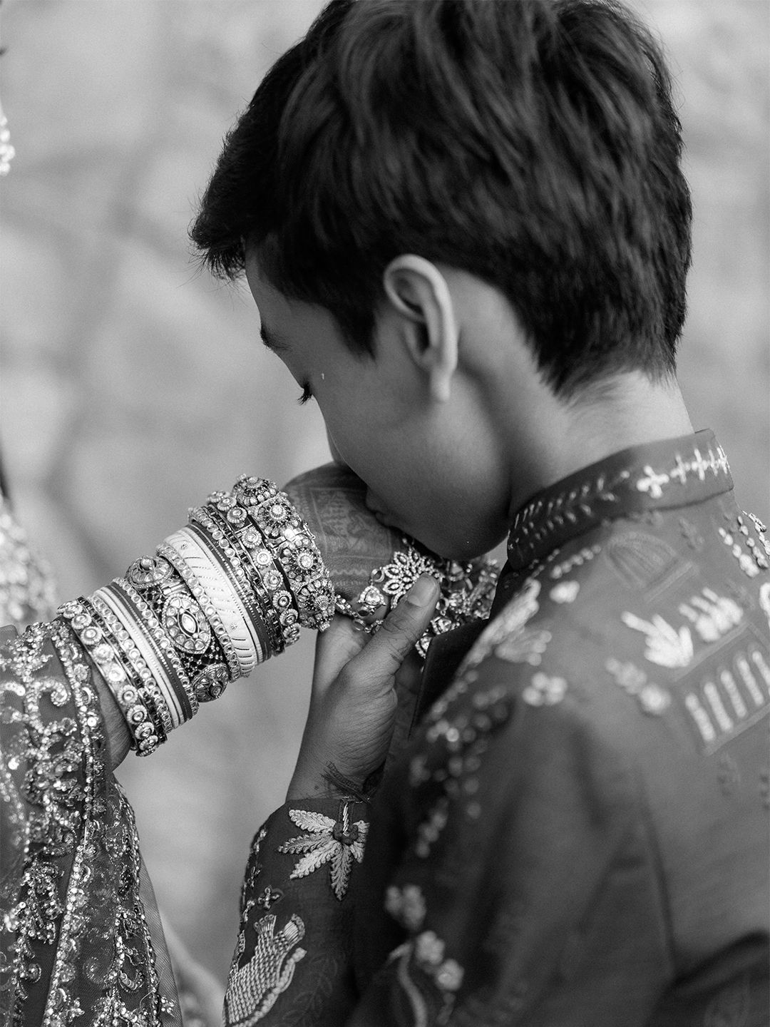 Black and white photo of groom kissing bride's bangles adorned hands at Indian wedding.