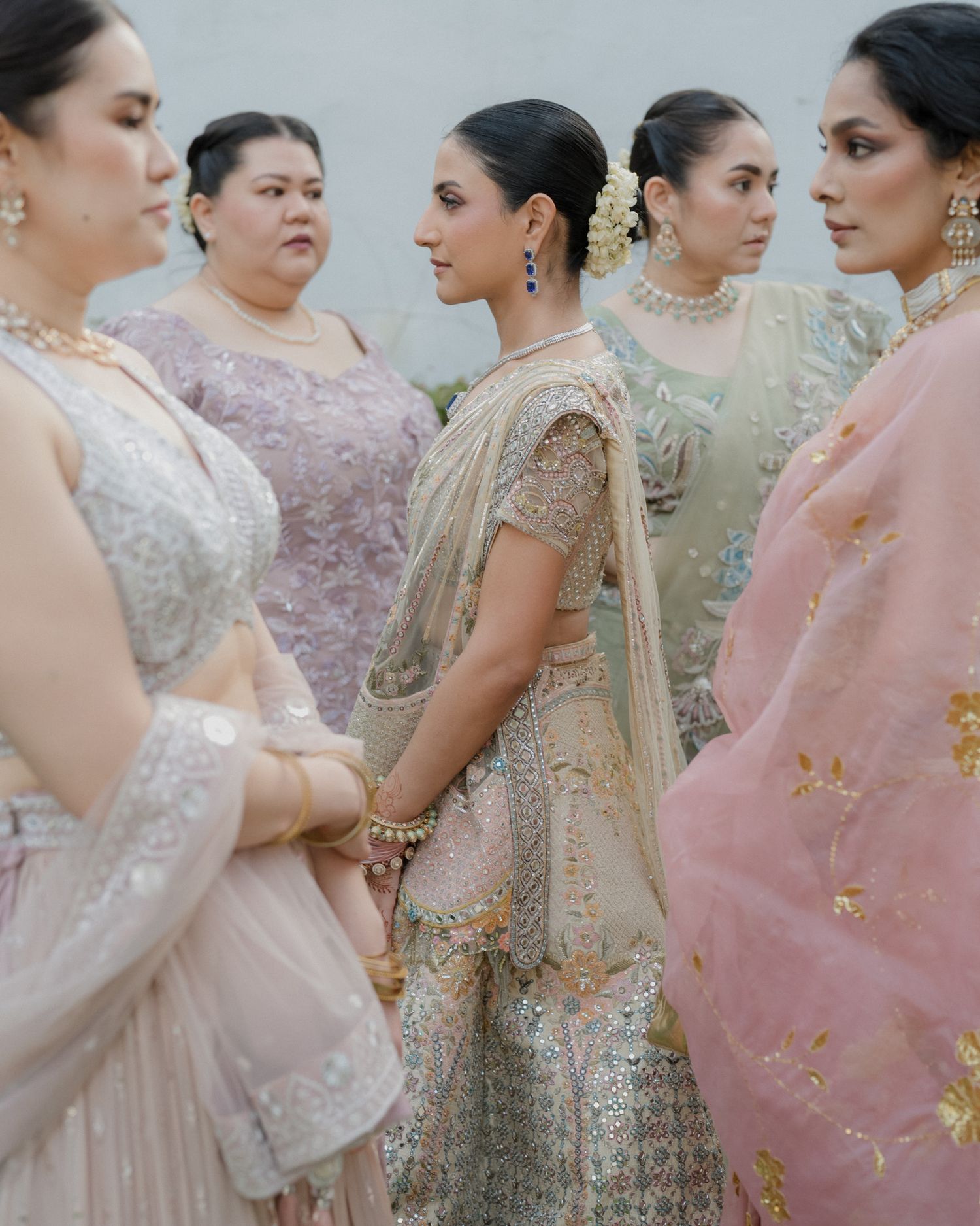 Indian bridesmaids in pastel embroidered lehengas and sarees with gold jewelry at wedding ceremony.