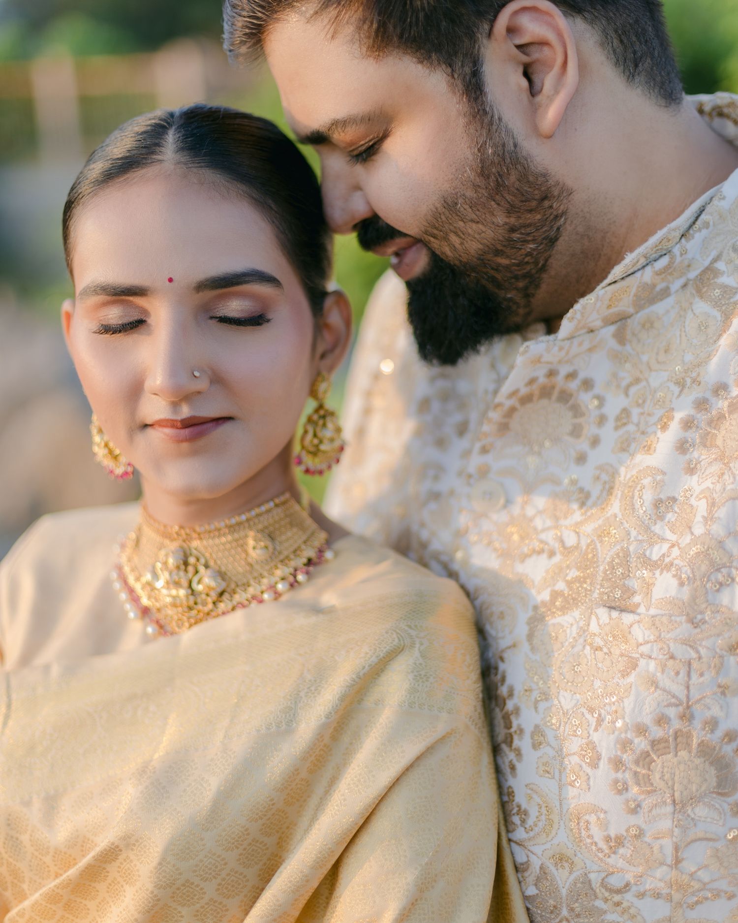Indian couple in golden outfits sharing an intimate moment, bride wearing traditional jewelry and nose ring.
