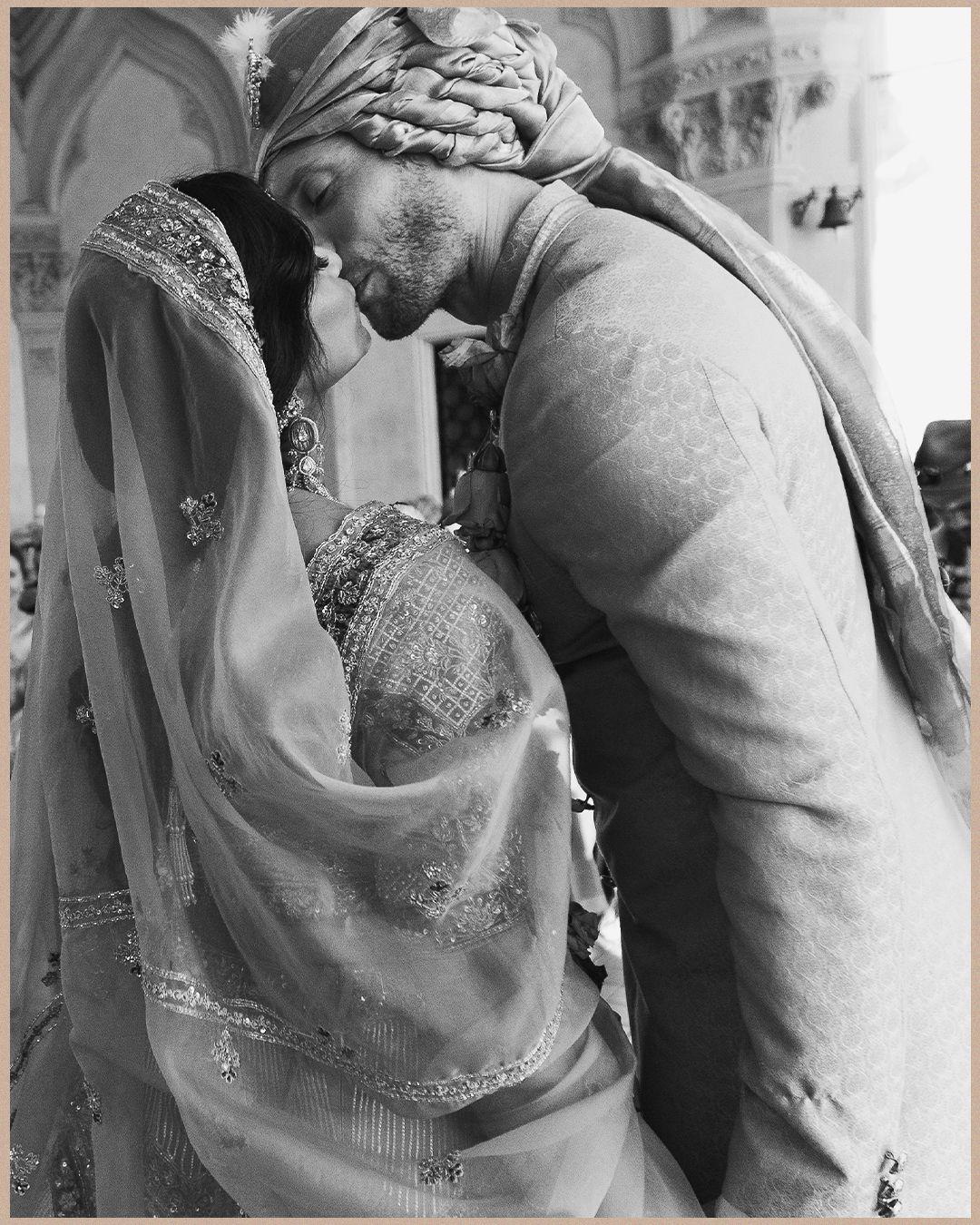 Black and white intimate moment of Indian bride and groom embracing during traditional wedding ceremony.