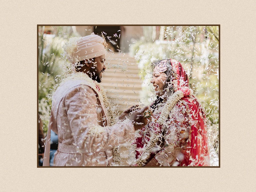 Indian bride and groom exchange garlands during jaimala ceremony showered with flower petals at royal wedding.