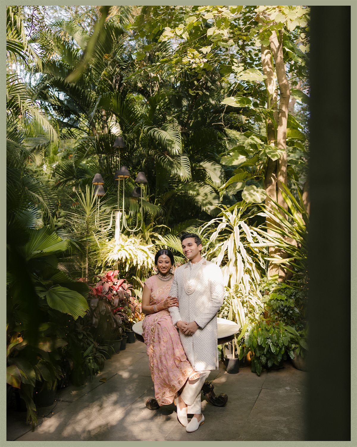 Indian wedding couple posing together in lush tropical garden setting.