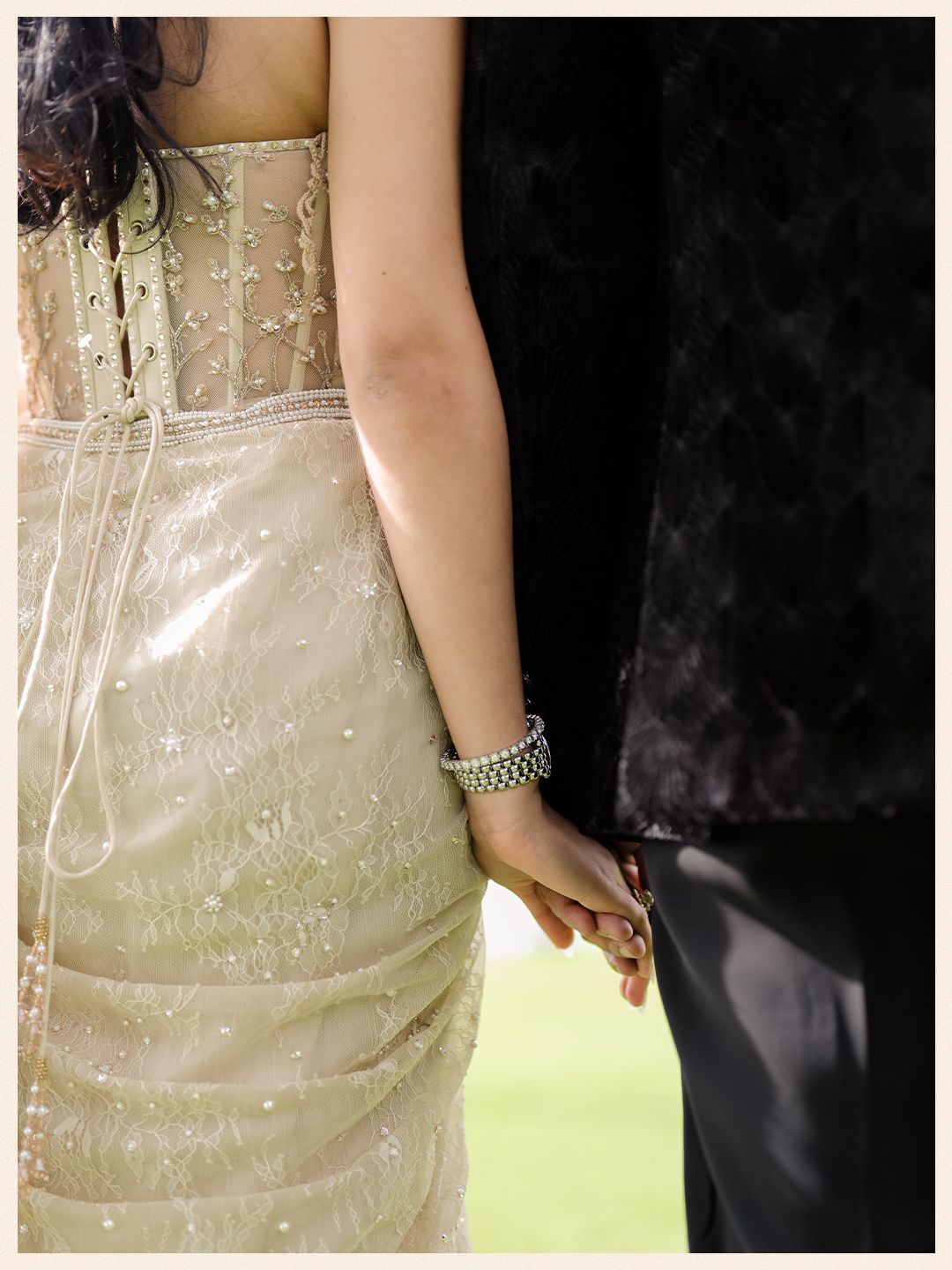 Close-up of bride in beaded ivory gown holding hands with groom in black velvet sherwani.