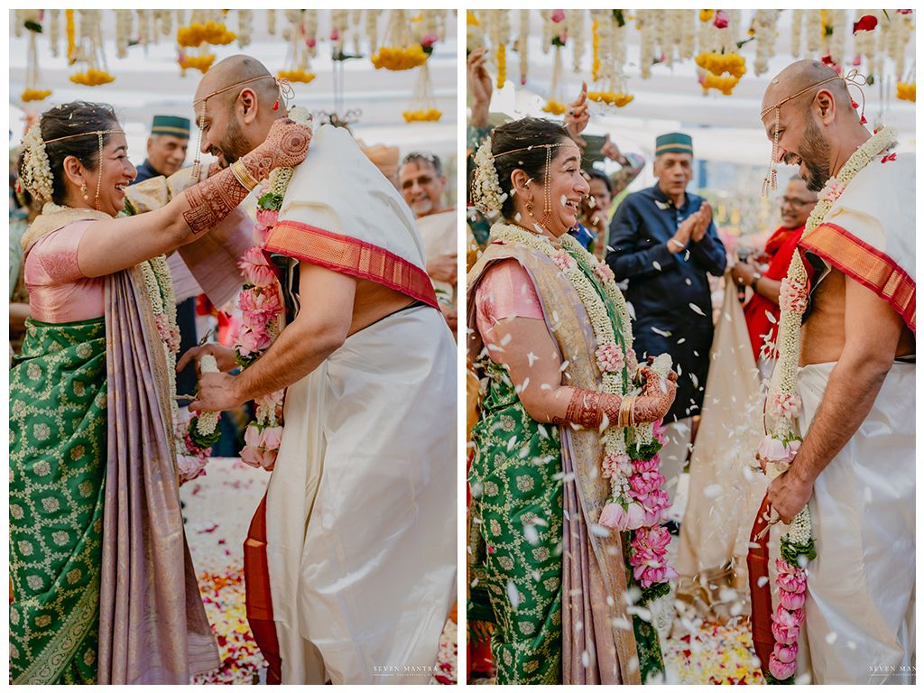 Indian bride and groom exchange garlands joyfully under floral mandap during wedding ceremony.