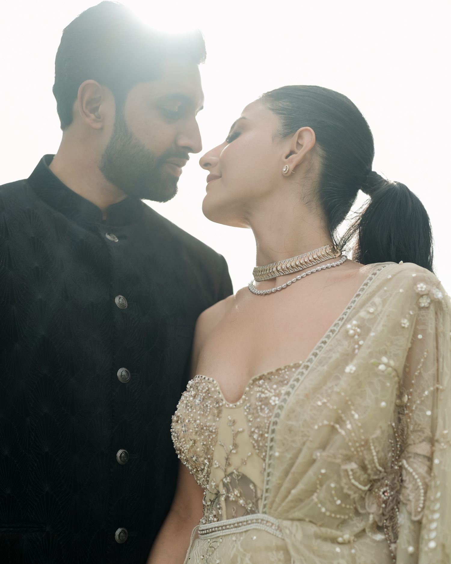 South Asian couple in black sherwani and gold embellished saree sharing romantic moment in soft backlight.