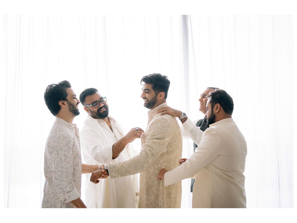 Groom gets ready with groomsmen adjusting his ivory sherwani before Indian wedding ceremony.