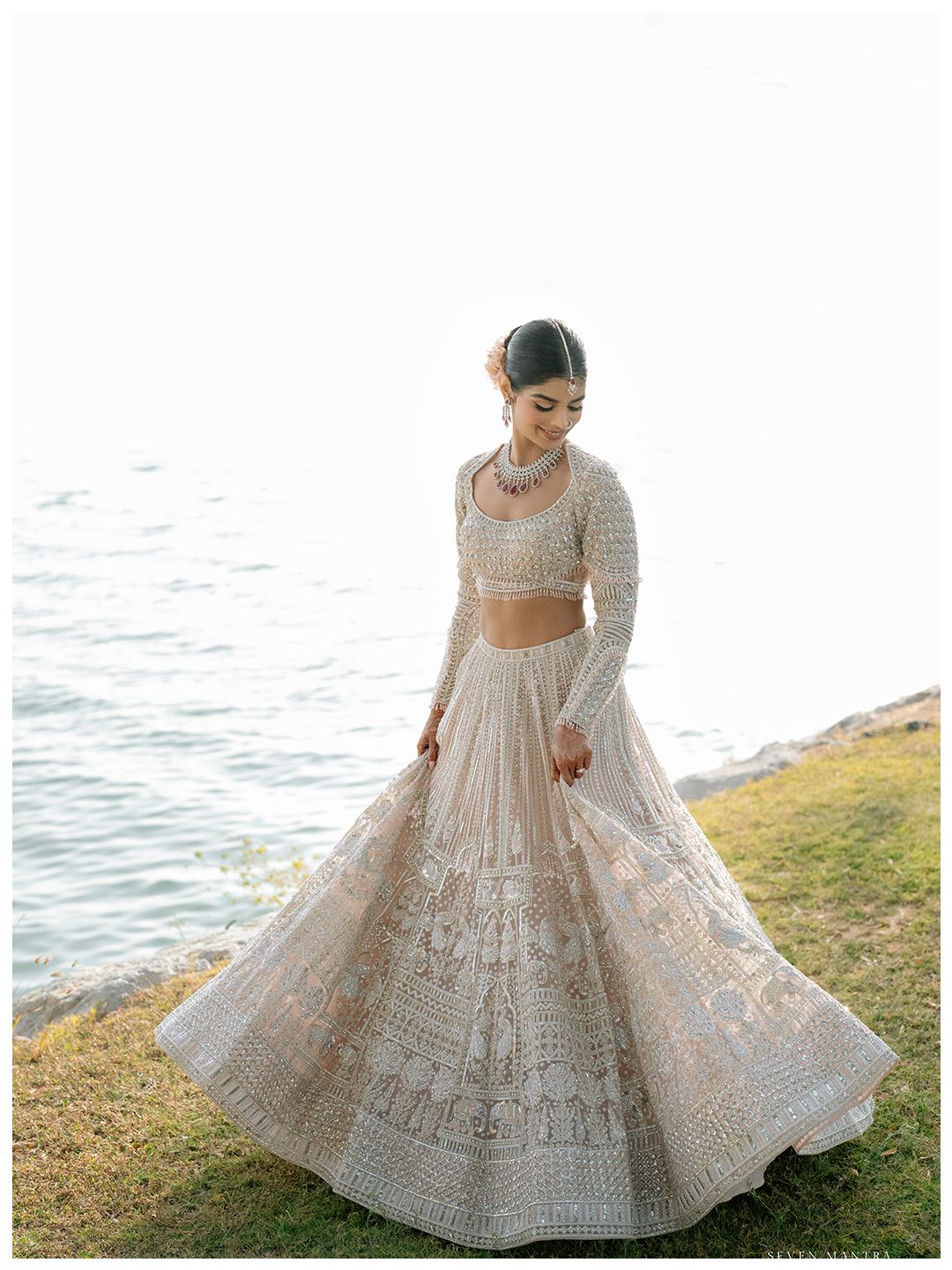 Bride twirls in stunning ivory embroidered lehenga by waterside for wedding portraits.