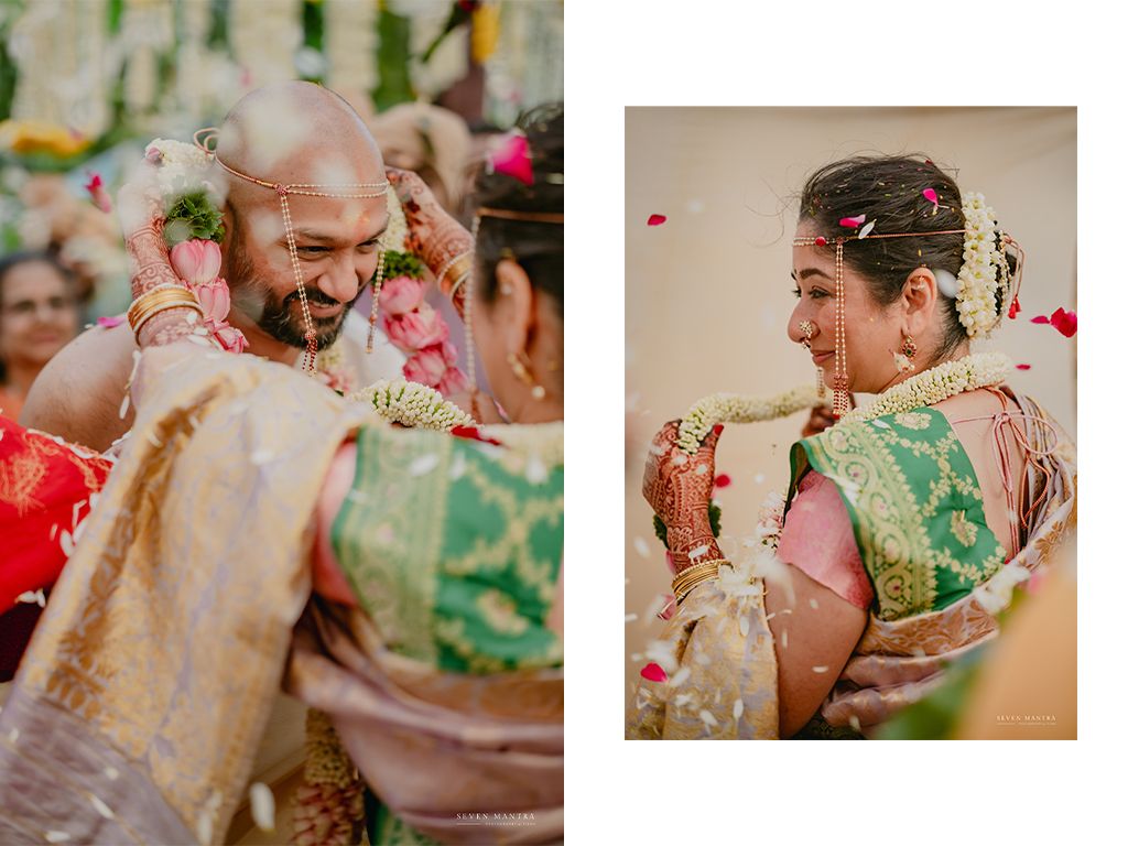 Indian groom places flower garland on bride amid colorful petals during traditional wedding ritual.