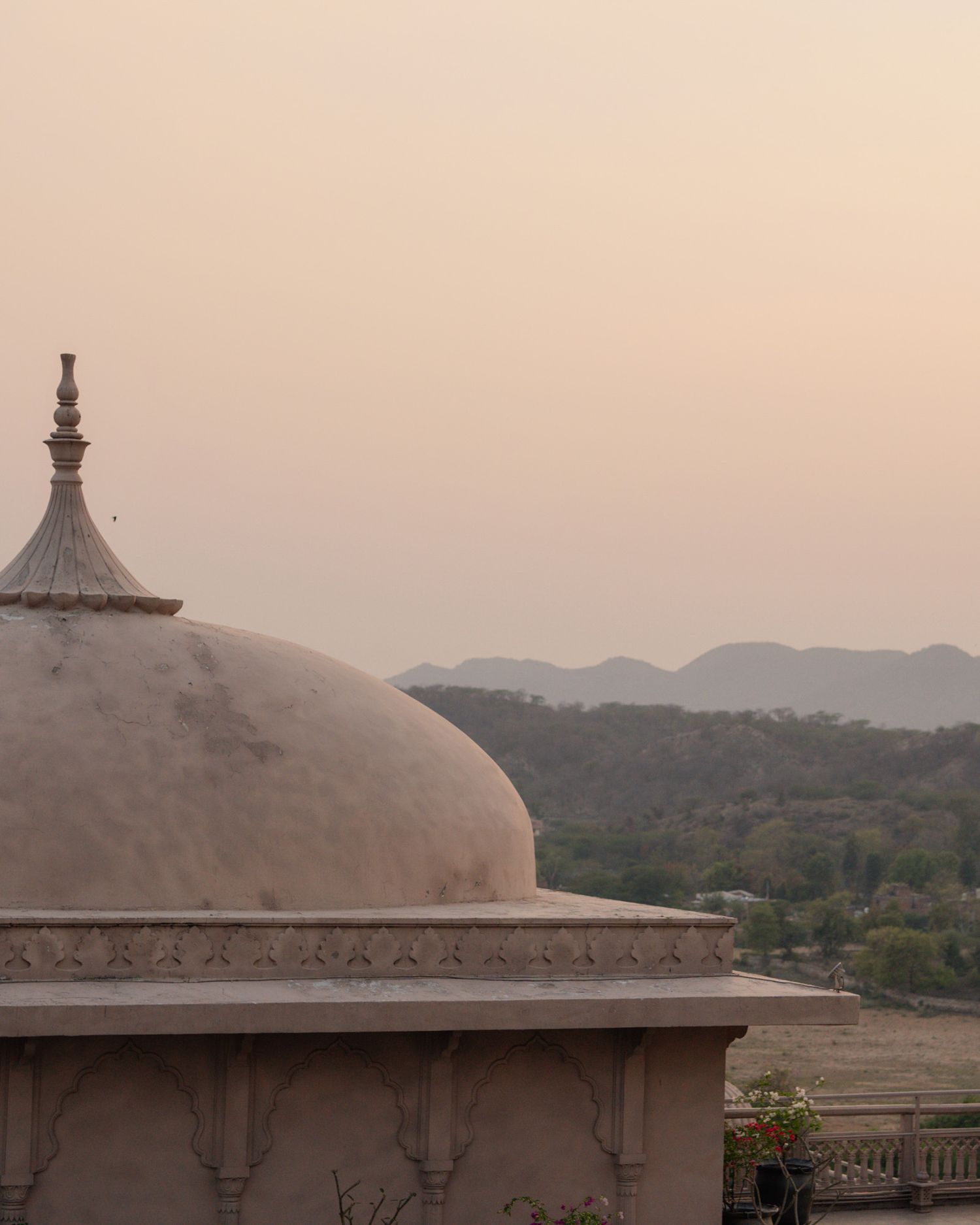 Elegant white domed Indian palace pavilion at sunset with misty mountain landscape backdrop.
