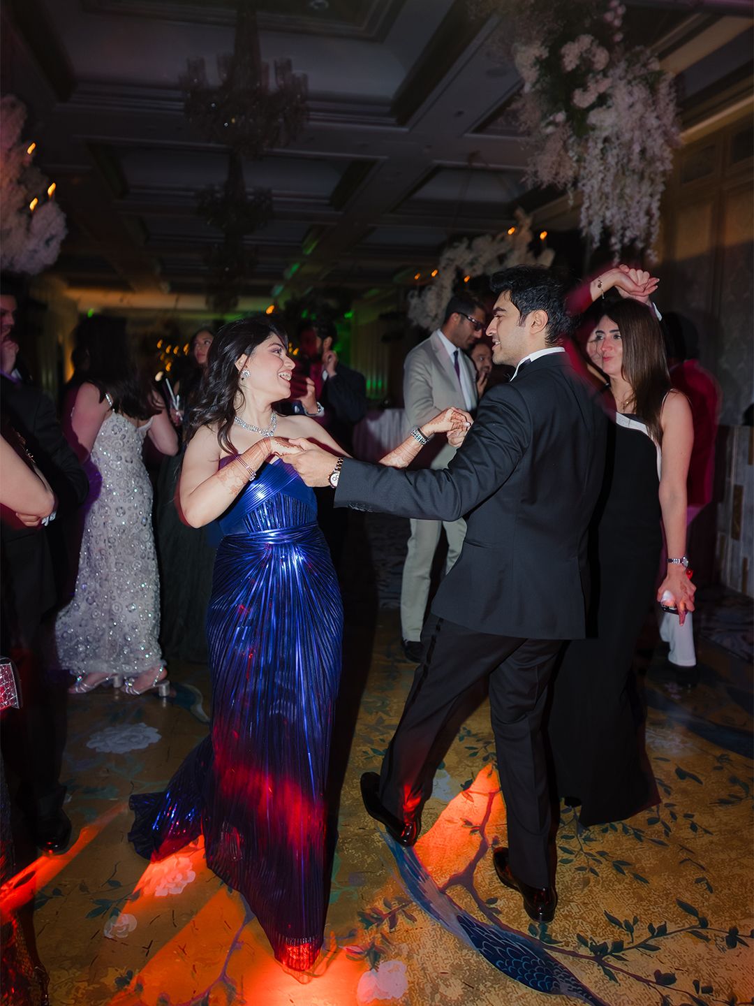 Couple dancing at Indian wedding reception, bride in blue sequin gown, groom in black tuxedo.