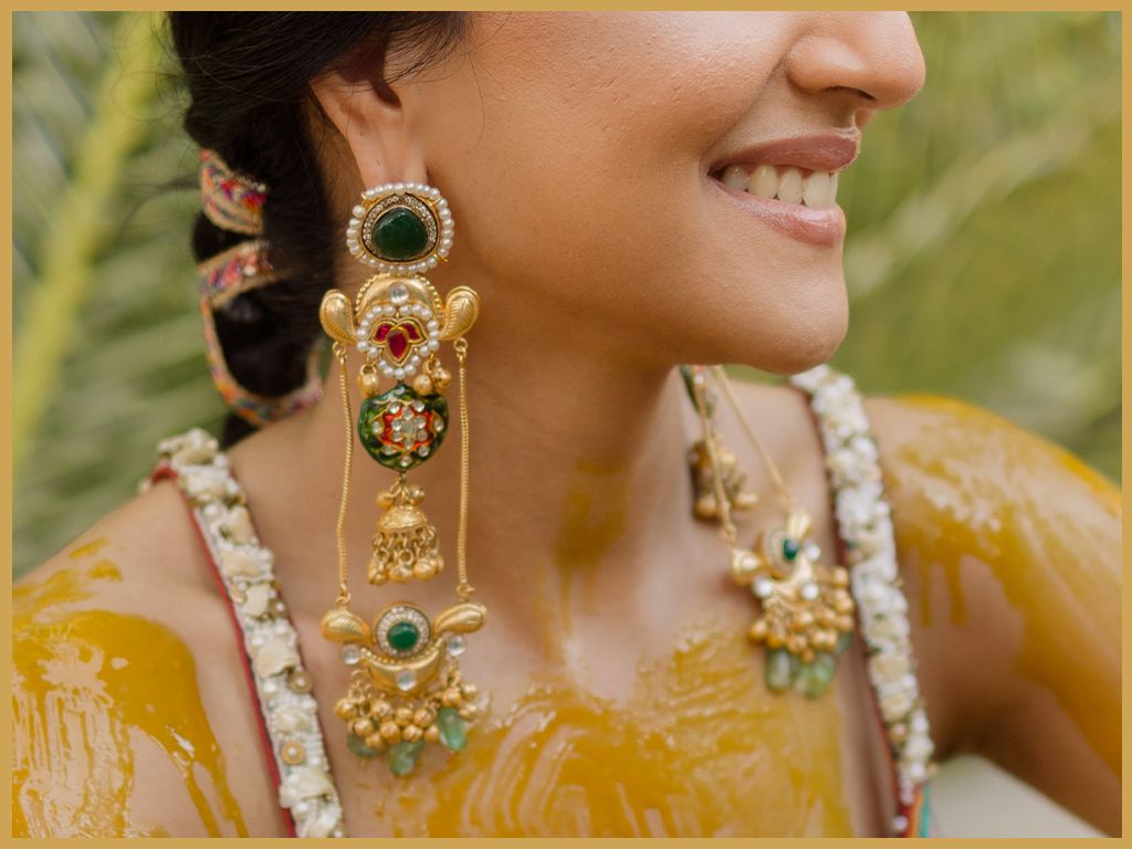 Bride smiling wearing ornate gold and green traditional Indian chandelier earrings with floral jewelry.