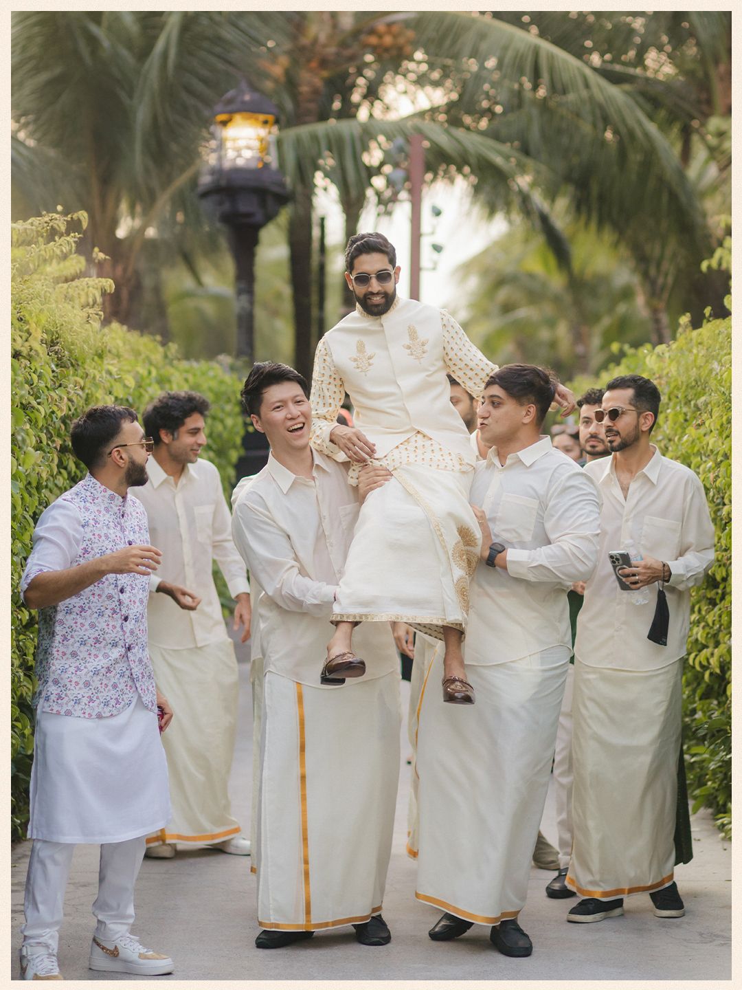 Groom lifted by groomsmen in white kurtas during a joyful Indian wedding baraat celebration outdoors.