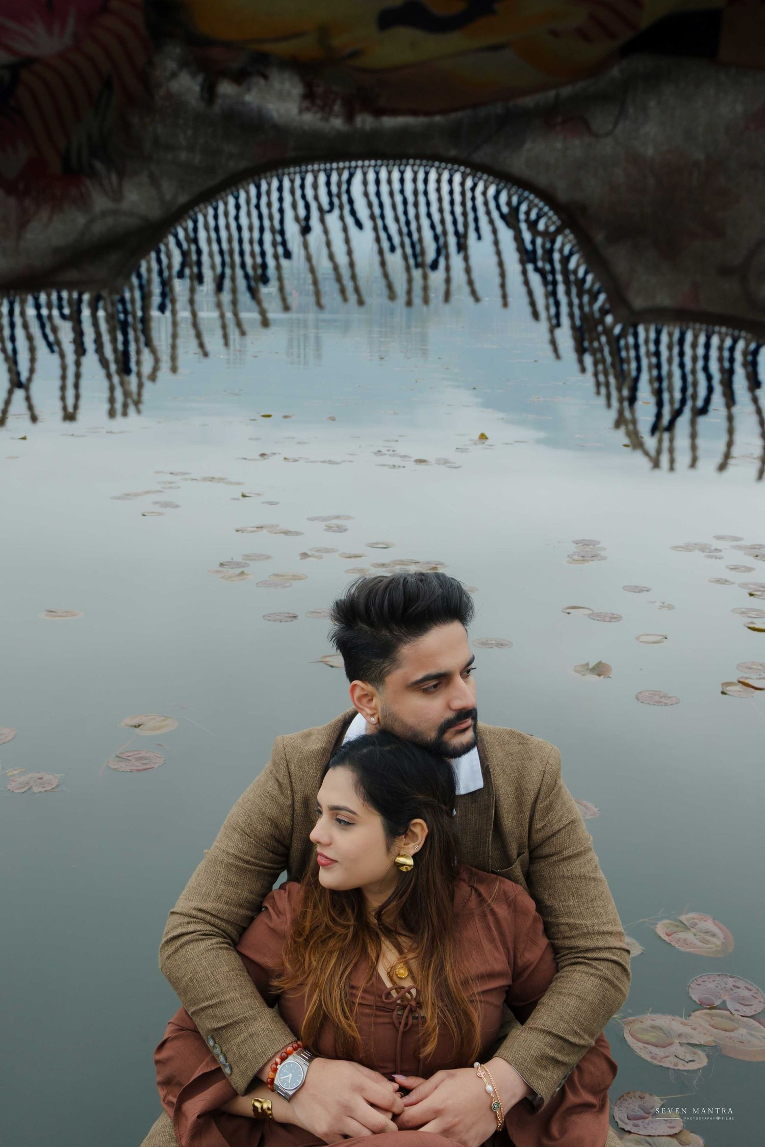 Romantic couple in traditional Indian attire posing near reflective water with artistic framing.