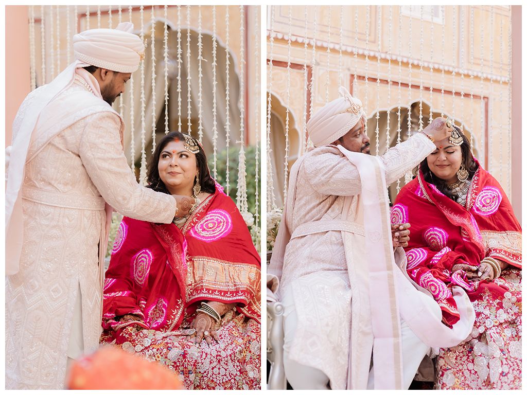 Groom applies sindoor to bride during traditional Indian wedding ritual in pink outdoor venue.