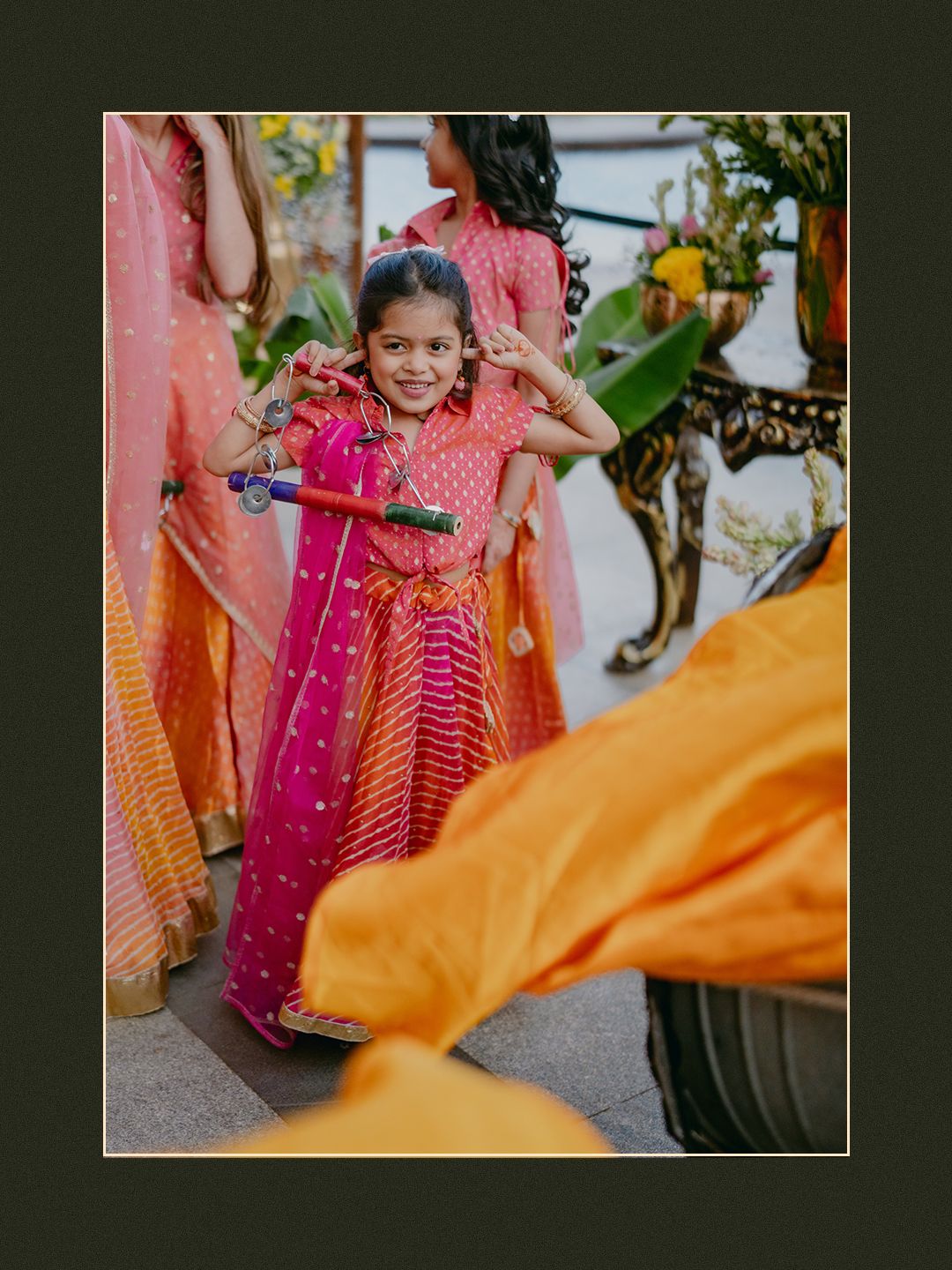 Adorable young girl in pink and orange lehenga smiling and posing during an Indian wedding celebration.