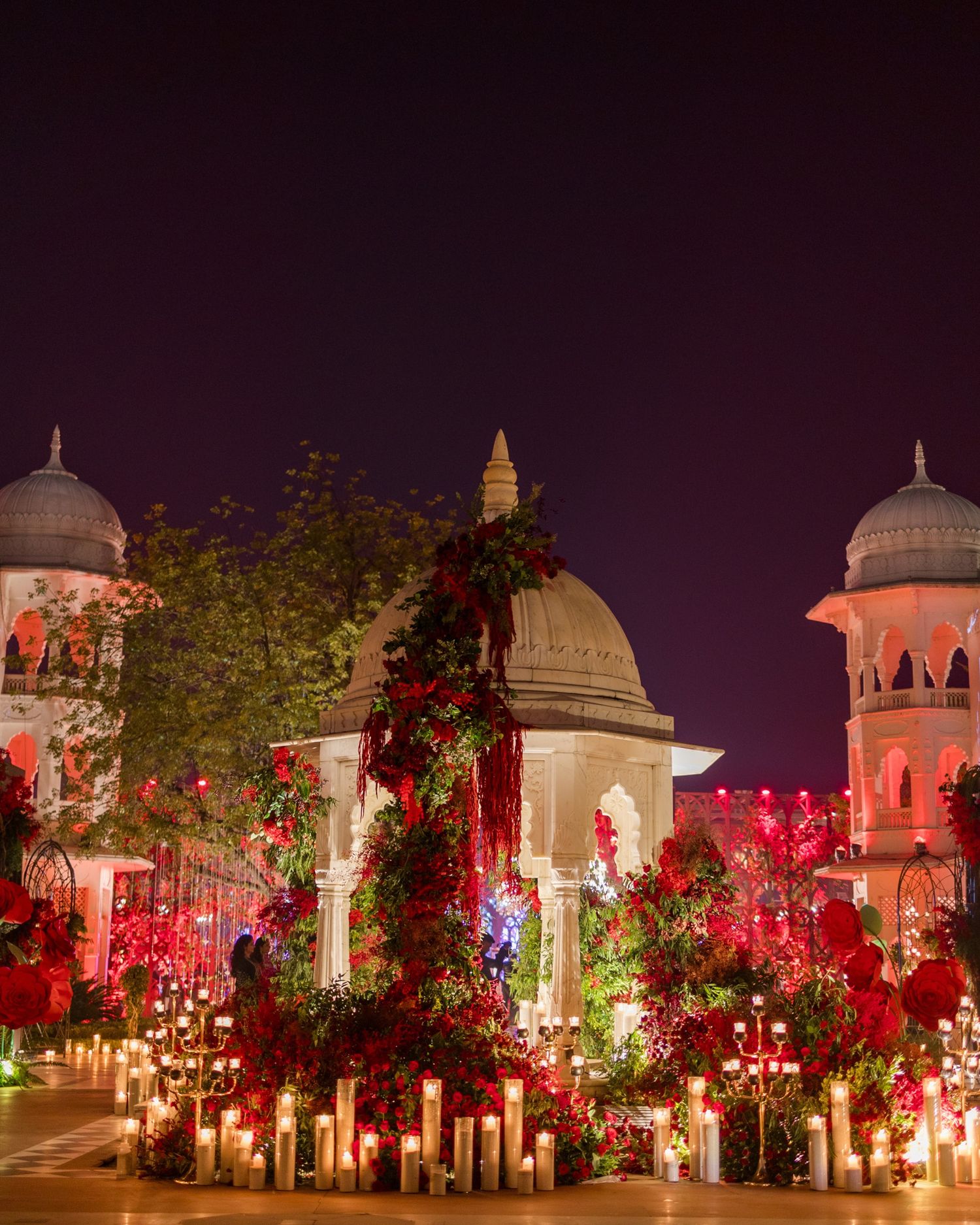 Stunning red floral wedding decor illuminates a grand palace venue at night.