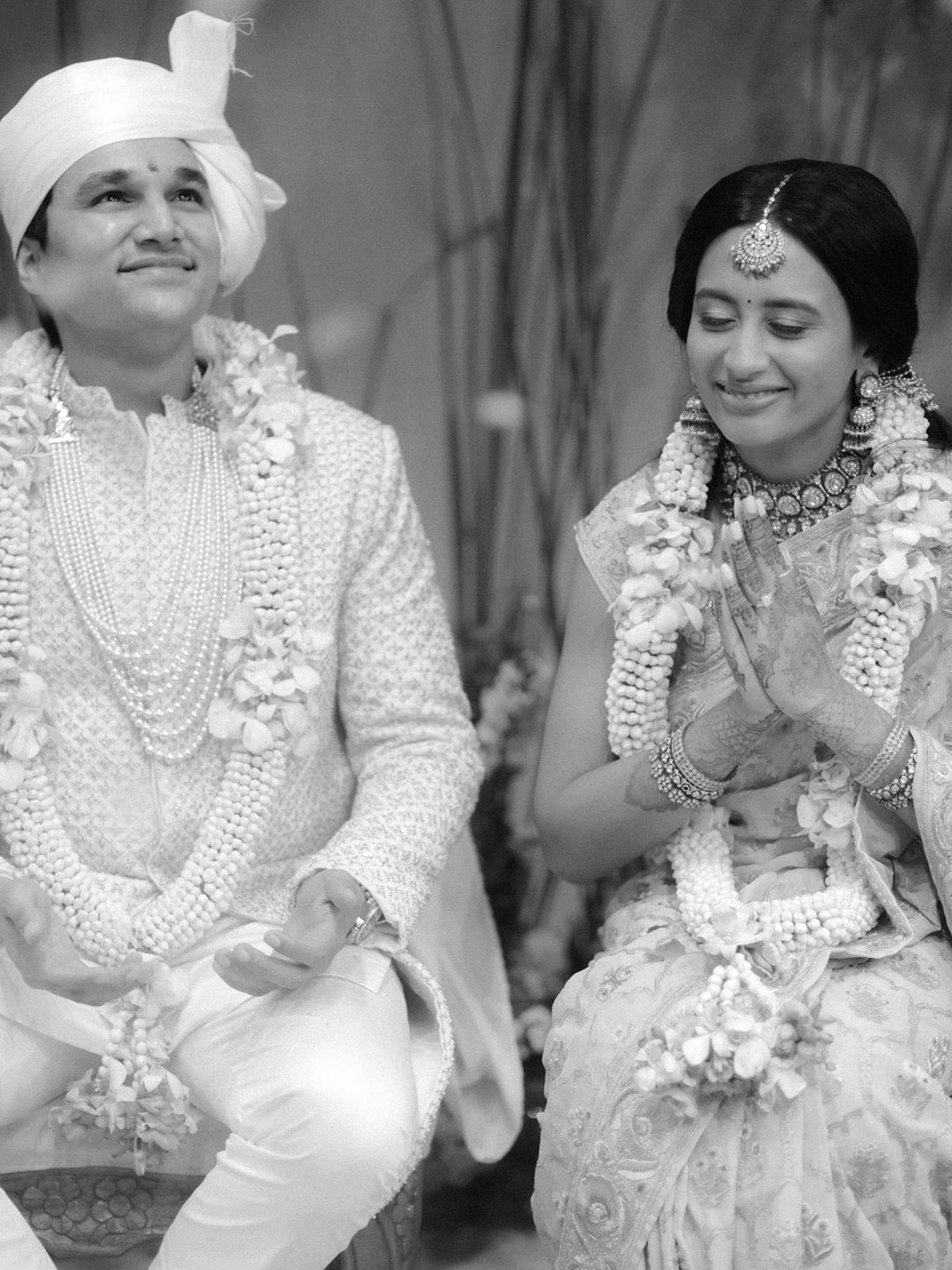 Black and white photo of smiling Indian bride and groom in white attire during wedding.