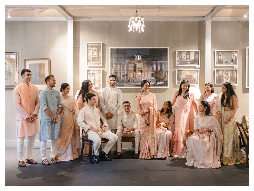 Indian wedding party posing in pastel outfits including sarees and sherwanis in elegant venue.