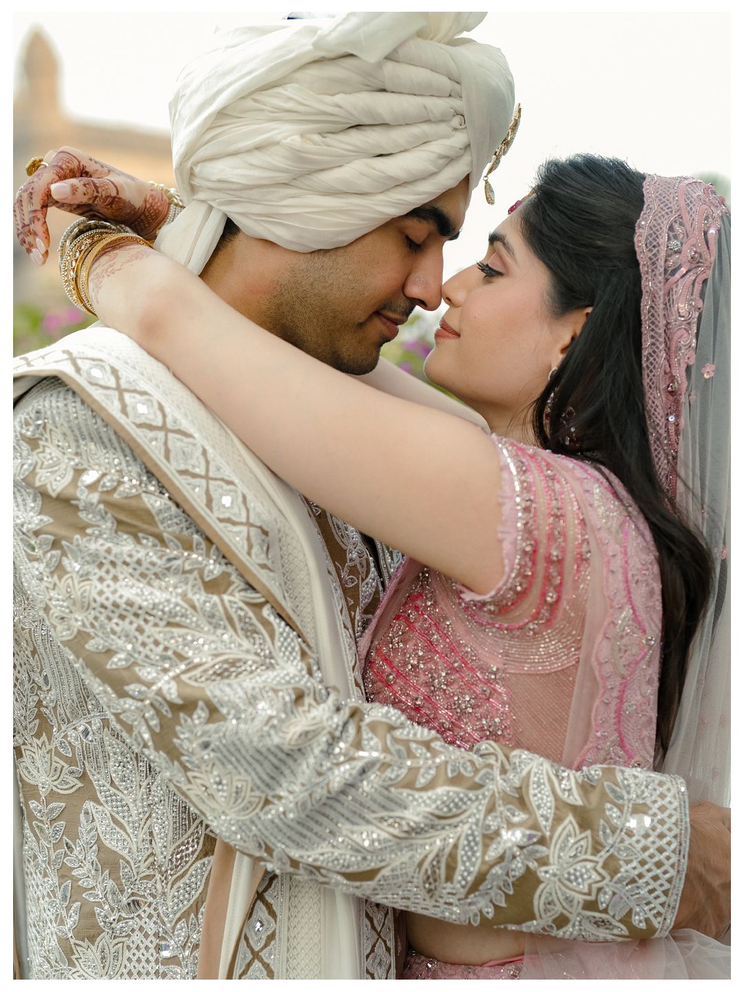 Indian bride and groom in elegant white embroidered wedding attire sharing an intimate romantic moment.