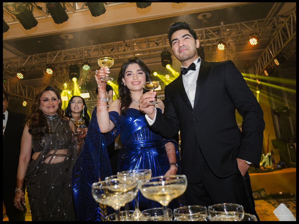 Couple toasting champagne at elegant Indian wedding reception in formal attire with champagne tower.