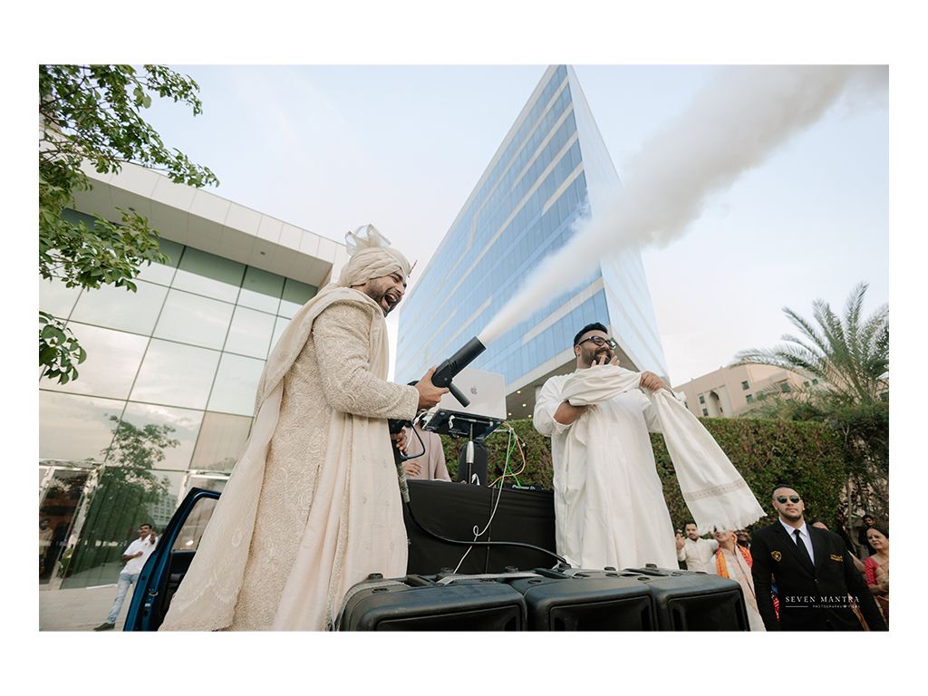 Groom arrives at Indian wedding baraat standing on car roof with smoke cannon.