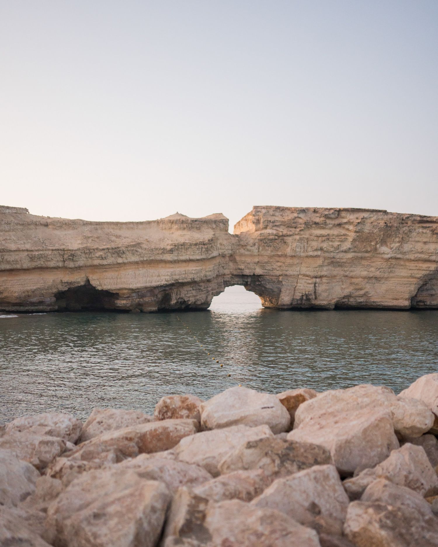 Dramatic natural rock arch over calm water with limestone cliffs and rocky shoreline in coastal landscape.