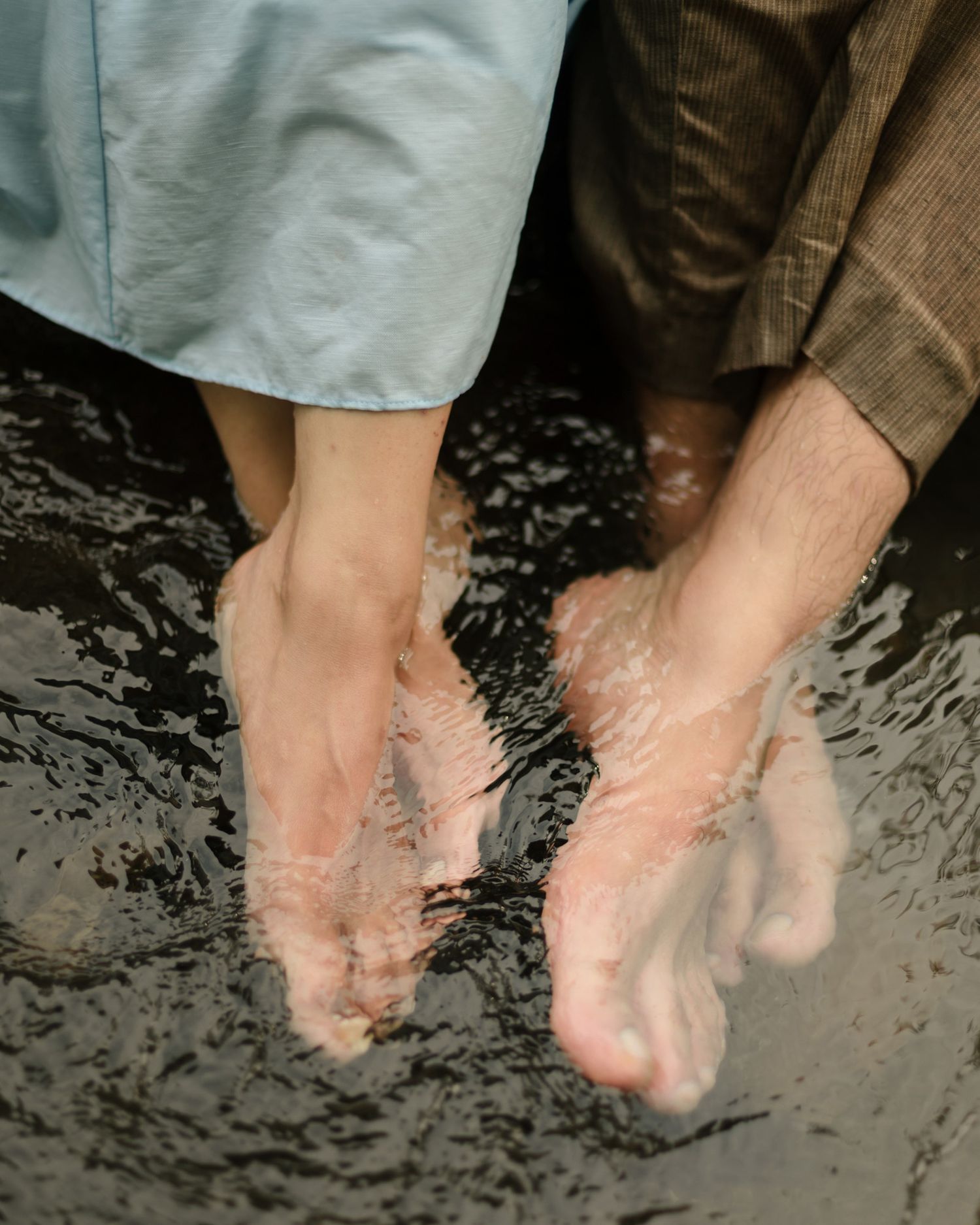 Close-up of couple's bare feet submerged in clear shallow stream water during photoshoot.