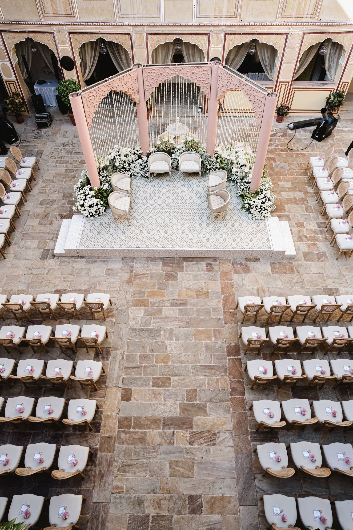 Aerial view of an elegant Indian wedding mandap setup in a royal courtyard with rows of white chairs.