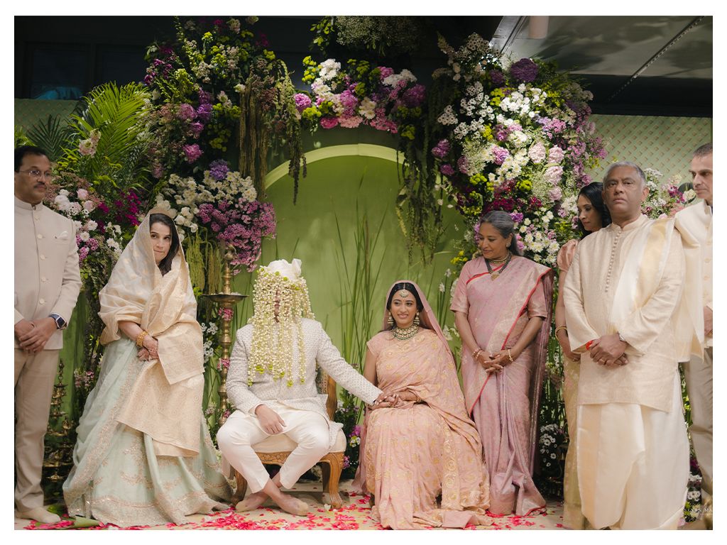 Indian bride and groom seated under floral mandap during traditional Hindu wedding ceremony.